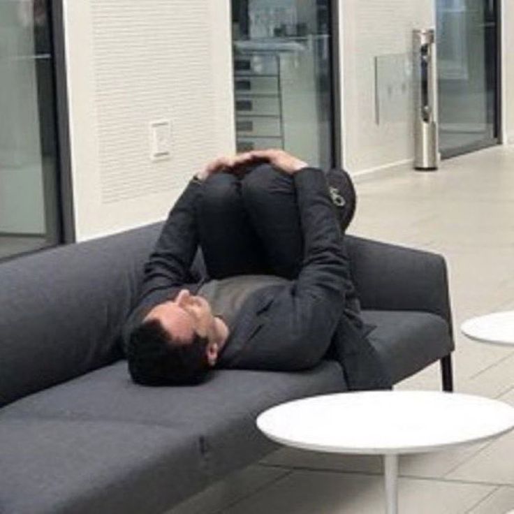 a man laying on top of a gray couch in a room filled with tables and chairs