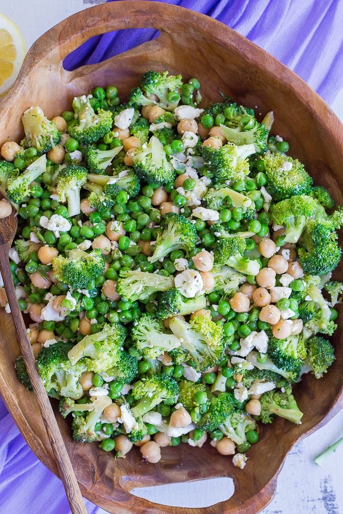 a wooden bowl filled with broccoli and chickpeas next to a lemon wedge