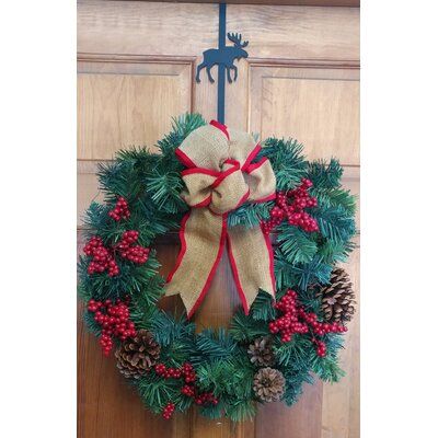 a christmas wreath hanging on a door with pine cones and red berries around the wreath