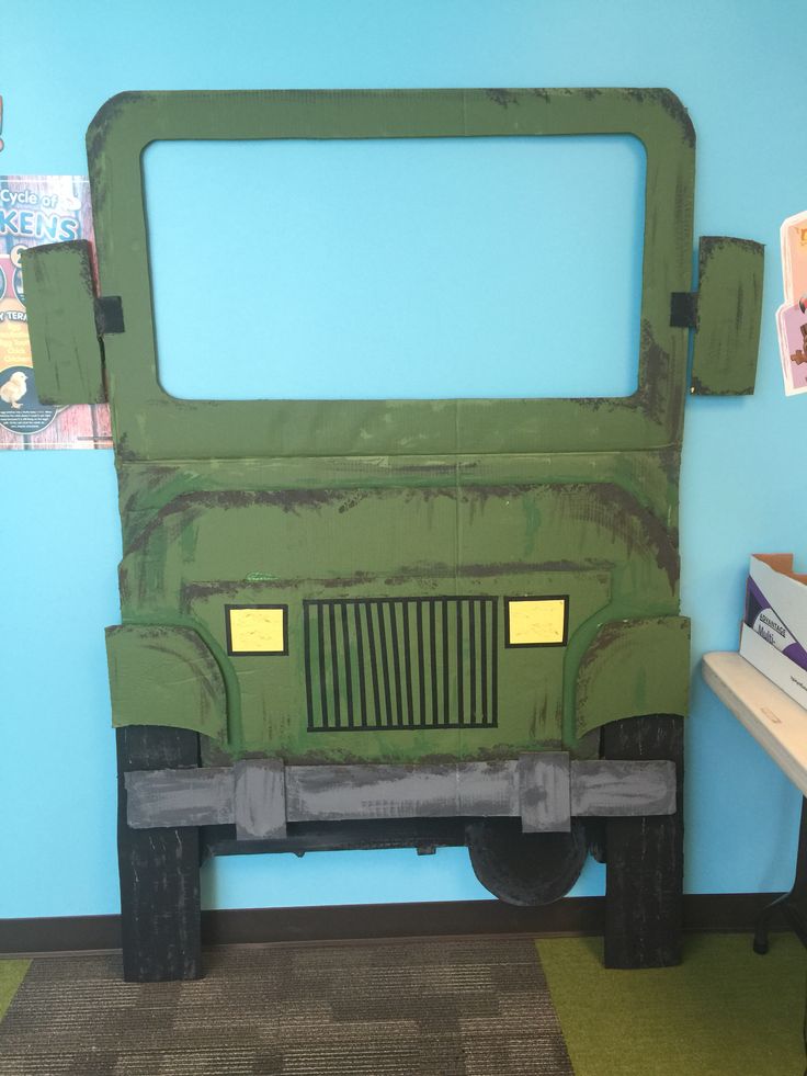 a green truck made out of cardboard sitting on top of a floor next to a blue wall