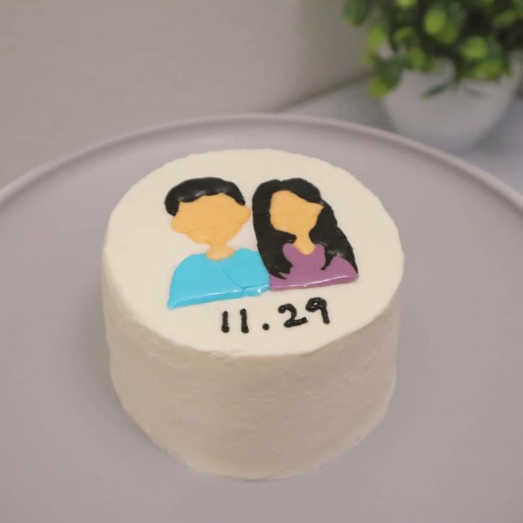 a white cake with two people on it sitting on a plate next to a potted plant