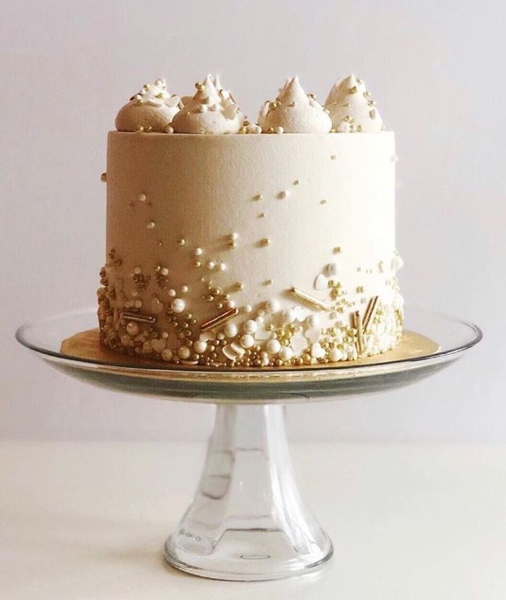 a cake with white frosting and gold sprinkles sits on a glass plate