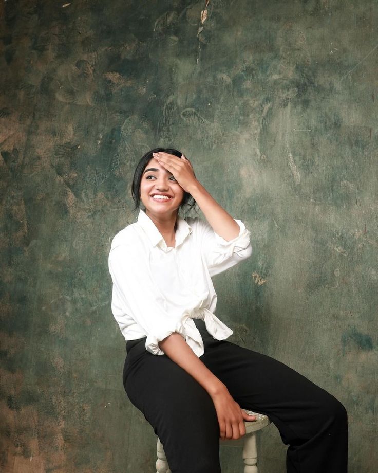 a woman sitting on top of a white chair next to a green wall and smiling