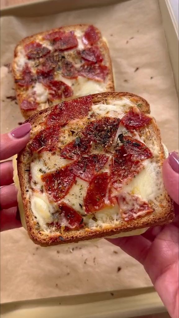 two pieces of bread with cheese and pepperoni on them are being held by someone's hand