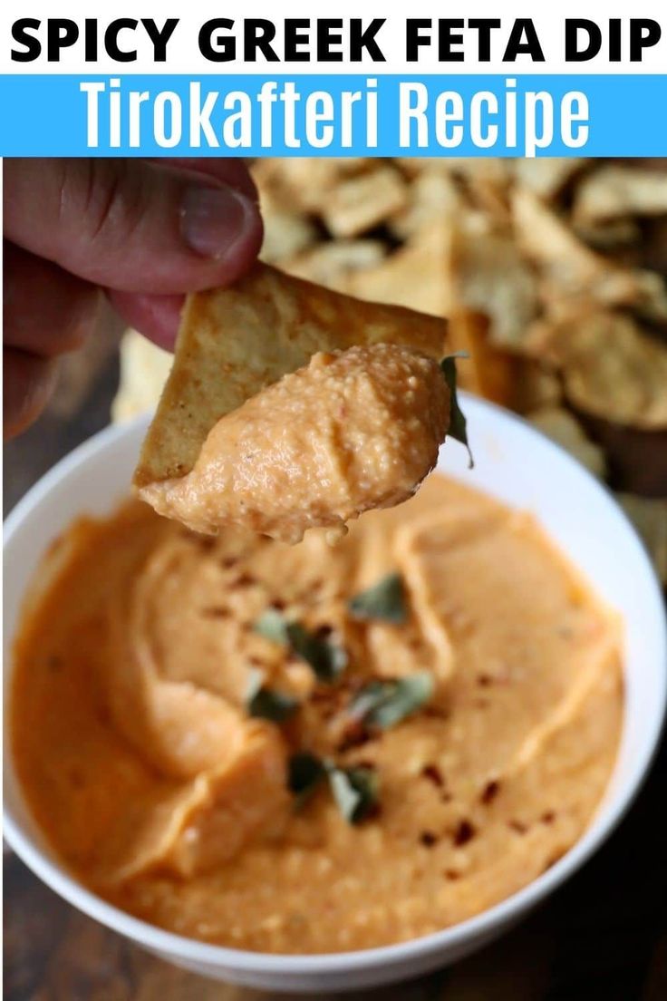 a hand holding a tortilla chip over a bowl of dip