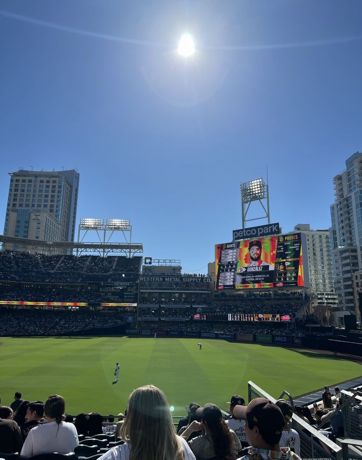 the sun is shining over a baseball field with people sitting in seats and watching it