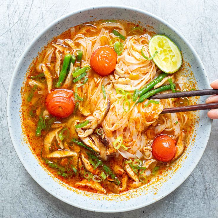 someone is holding chopsticks over a bowl of noodles and vegetables with tomatoes on the side