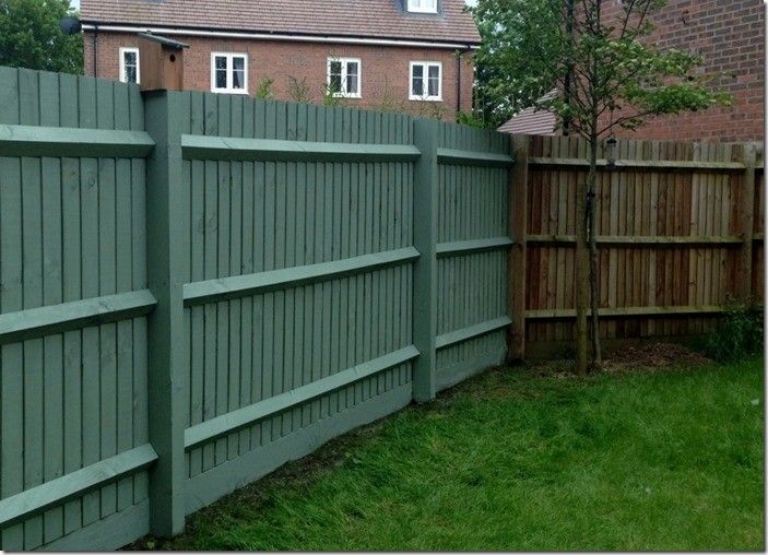 a wooden fence in front of a brick building and green grass with a bench next to it