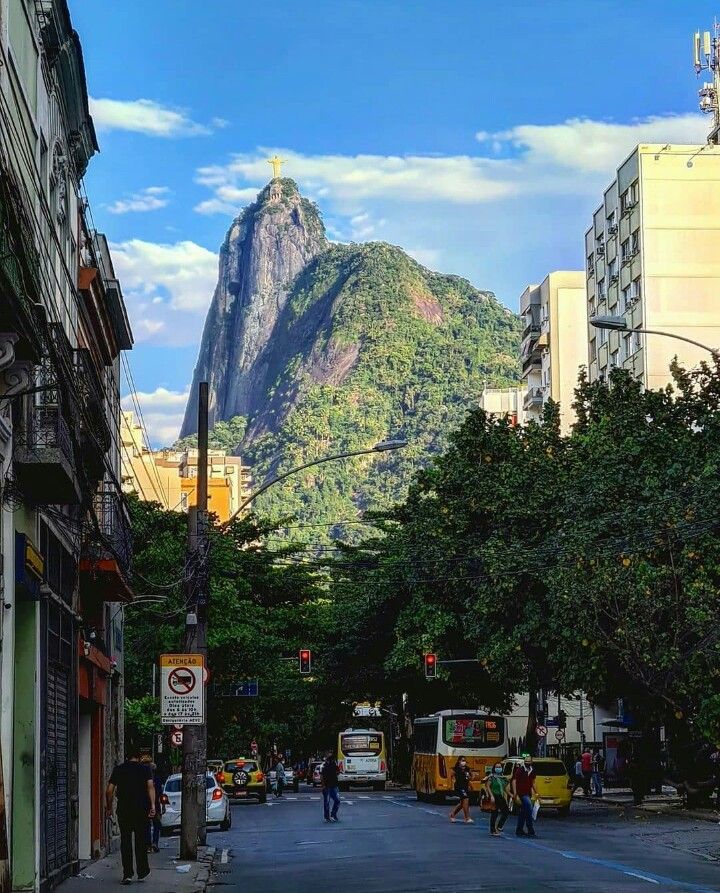 people are walking down the street in front of tall buildings with mountains in the background