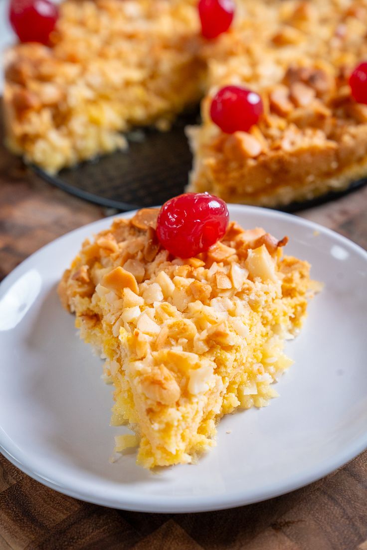 a piece of cake on a white plate with a cherry on top and another slice in the background