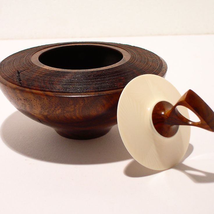 a wooden bowl with a white lid next to a brown and white ceramic cup holder