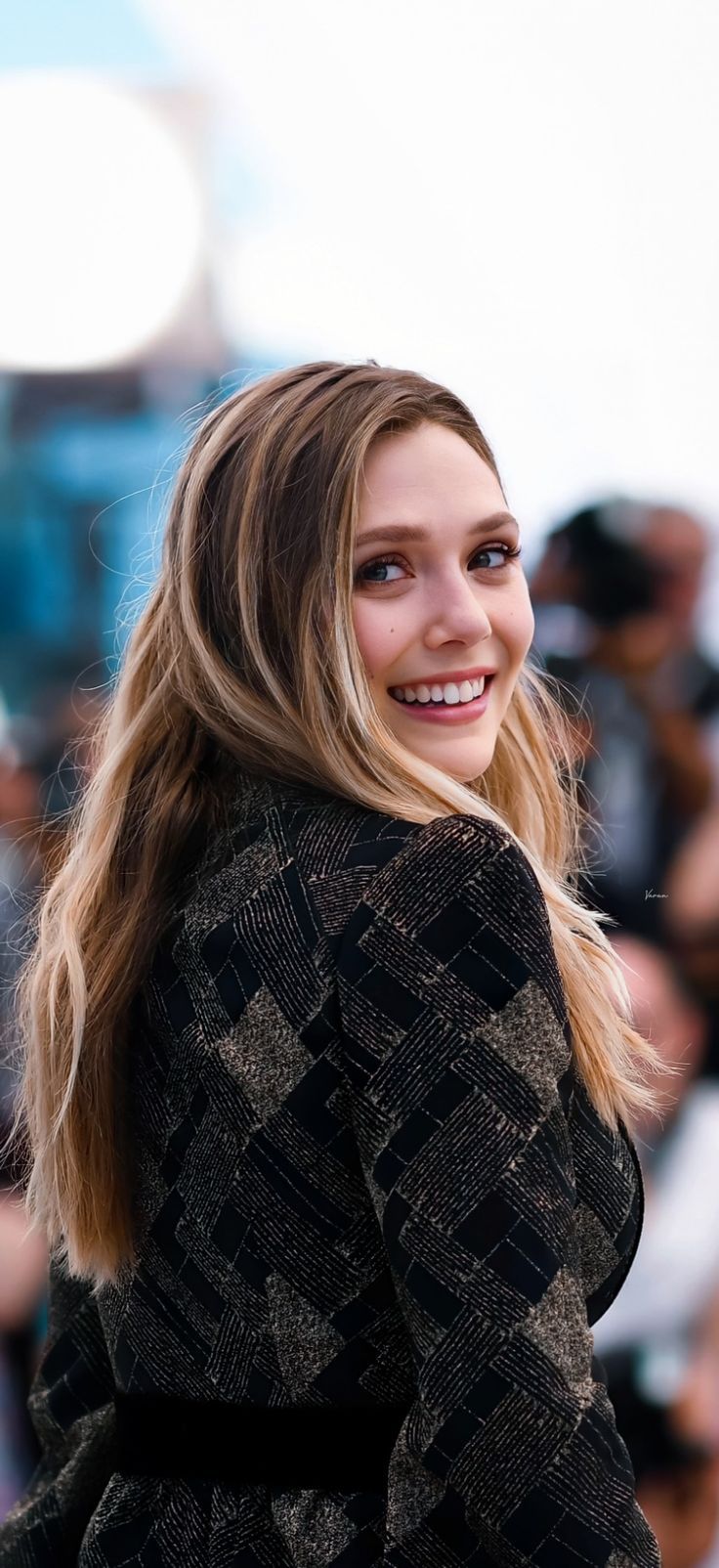 a woman standing in front of a crowd with her hair blowing back and smiling at the camera