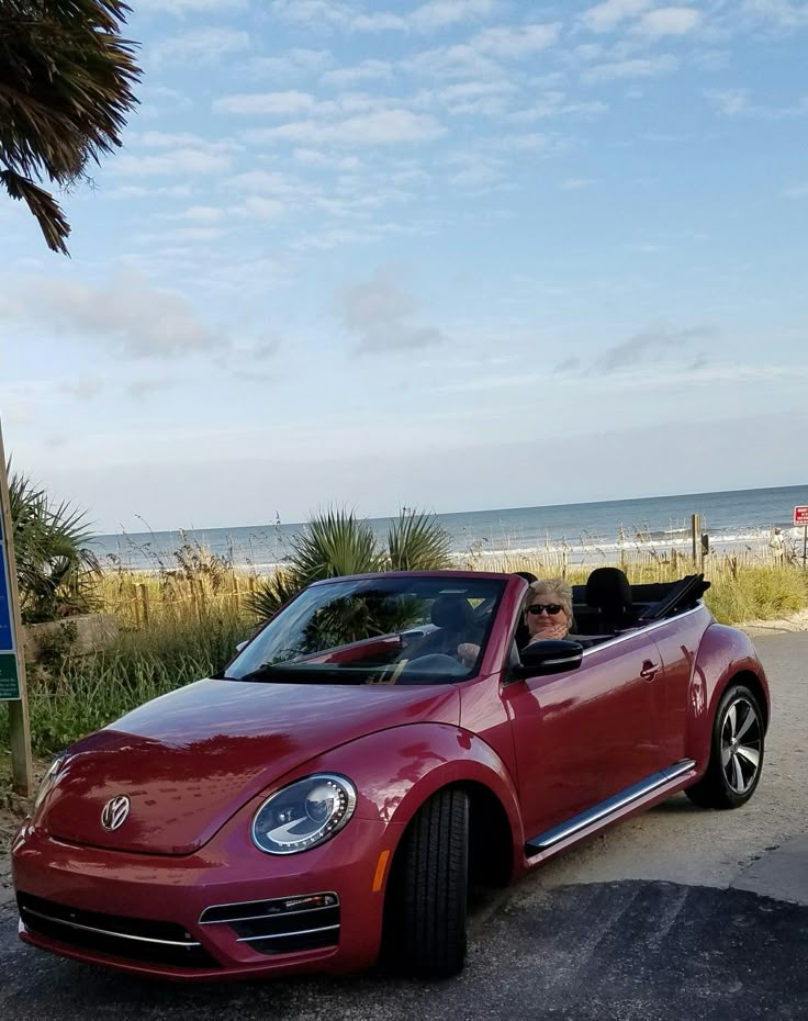 a red convertible car parked next to a beach