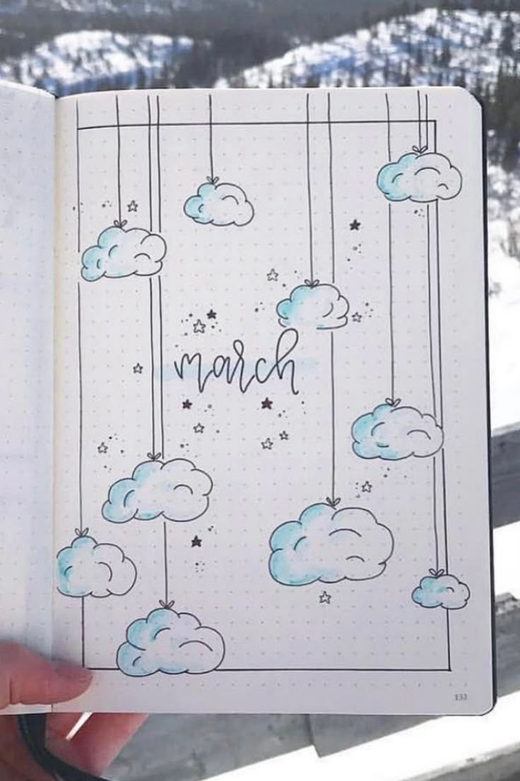 someone holding up a notebook with clouds and the word march written on it in blue ink