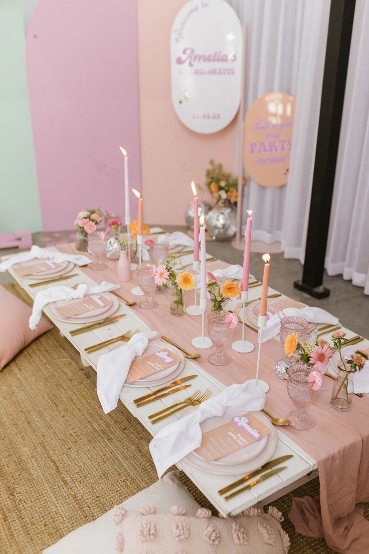 a table set up with pink and gold plates, napkins, candles and flowers