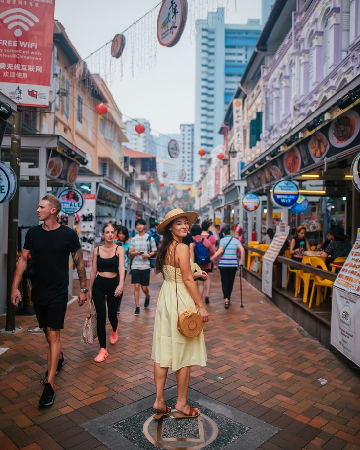 a woman in a yellow dress and hat standing on the street with people walking by