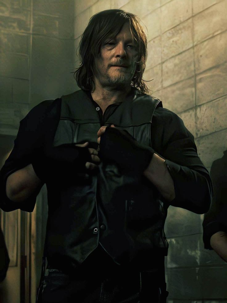 a man with long hair wearing a black shirt and holding his hands in his pockets