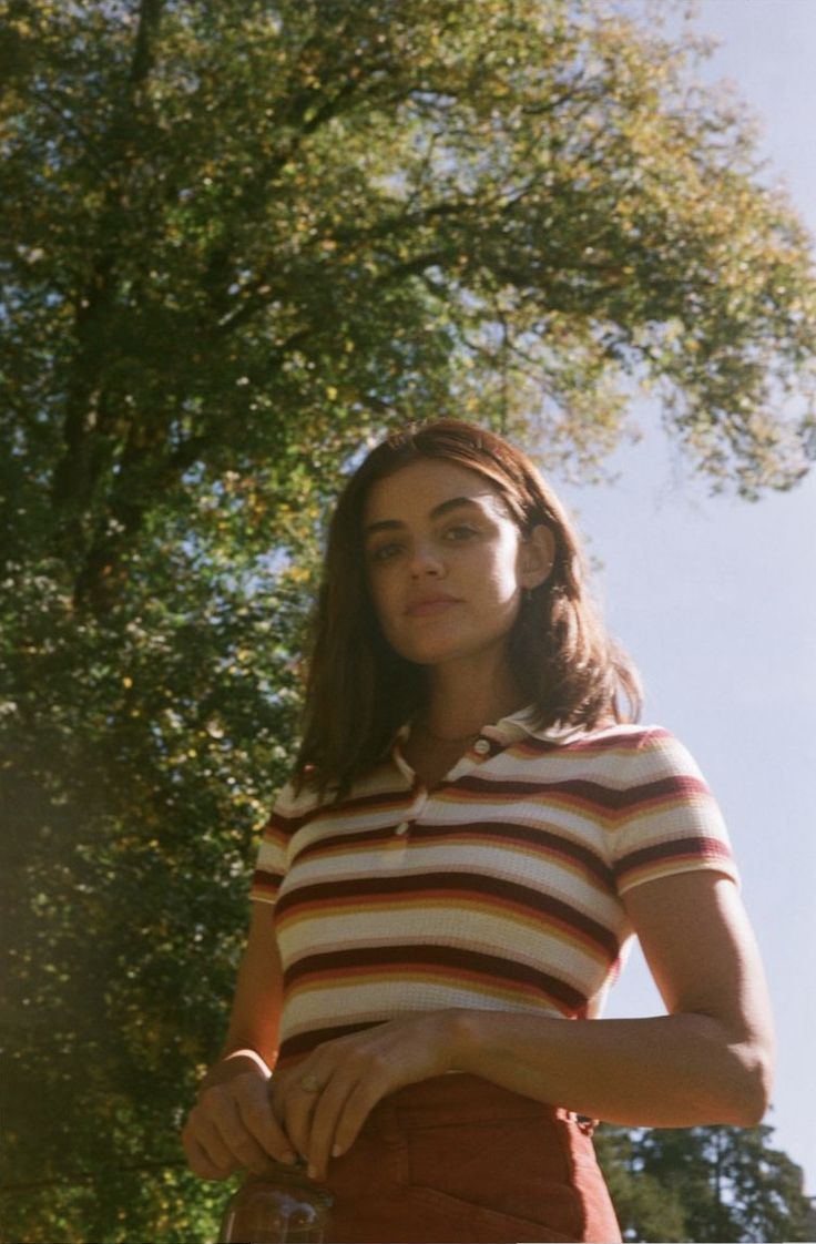 a woman standing in front of a tree with her hands on her hips and looking off to the side