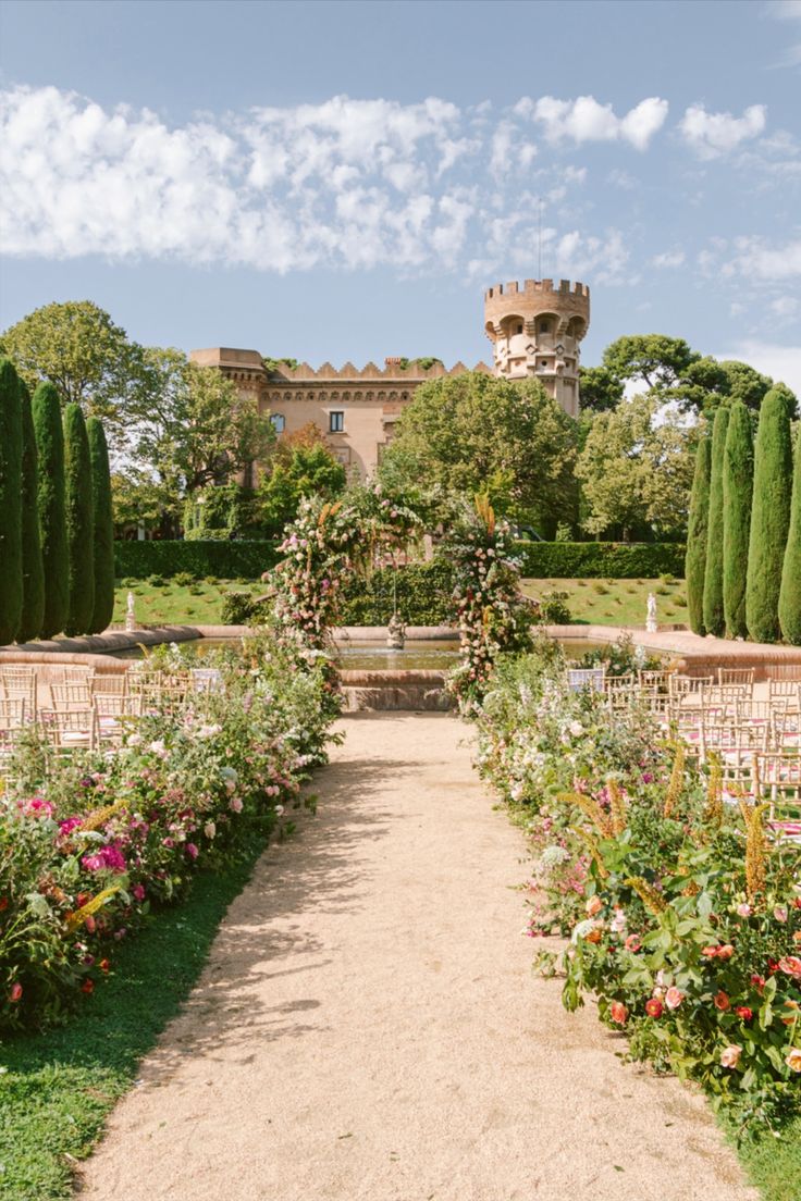 a garden with lots of flowers and trees in front of an old castle like building