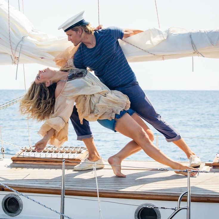 a man and woman are dancing on a sailboat in front of the ocean,