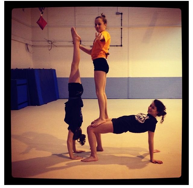 two girls doing acrobatic exercises in an indoor gym with one girl standing on her head