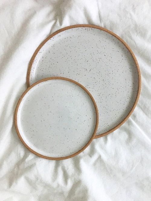 two white plates sitting on top of a bed next to each other with brown trim