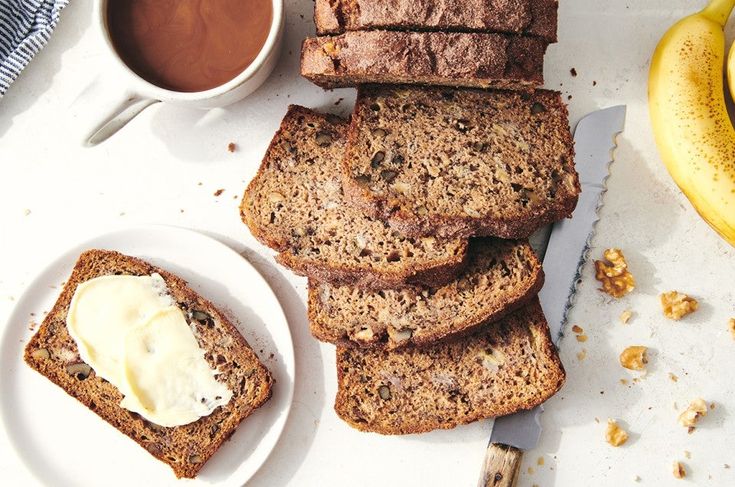 slices of banana bread with butter on a plate next to two bananas and a knife