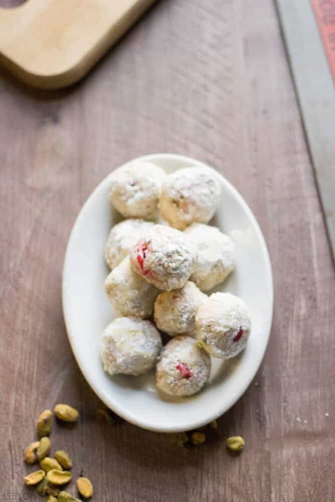 a white plate topped with snowball cookies and pistachios