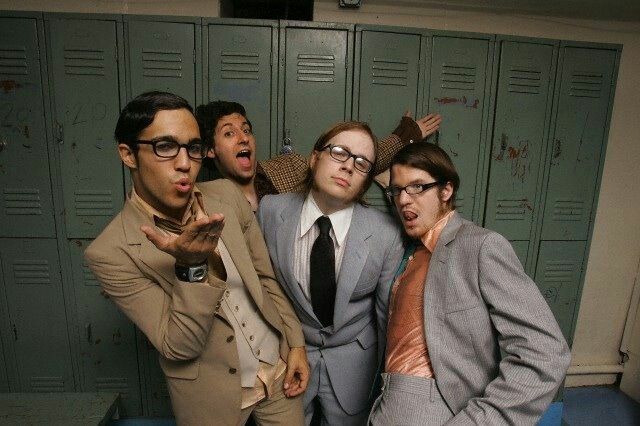 four men in suits and ties posing for the camera with their mouths open while standing next to lockers