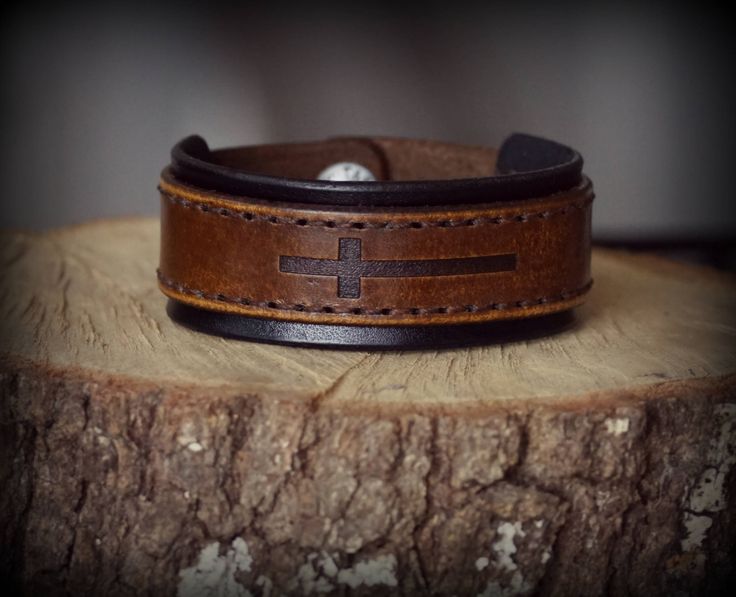 a leather bracelet with a cross on it sitting on top of a tree stump in front of a wall