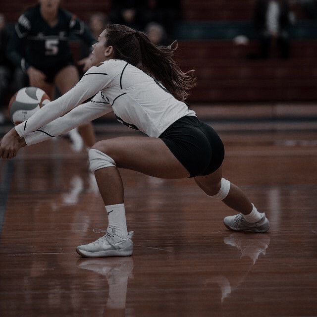 a female volleyball player is reaching for the ball while another girl watches from the sidelines