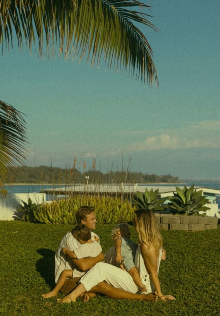 three people sitting on the grass talking to each other and one person holding a baby