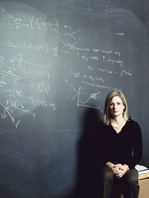 a woman sitting in front of a blackboard with writing on it