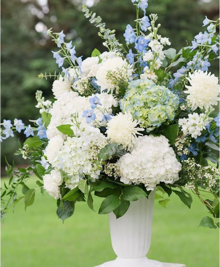 a white vase filled with blue and white flowers on top of a grass covered field