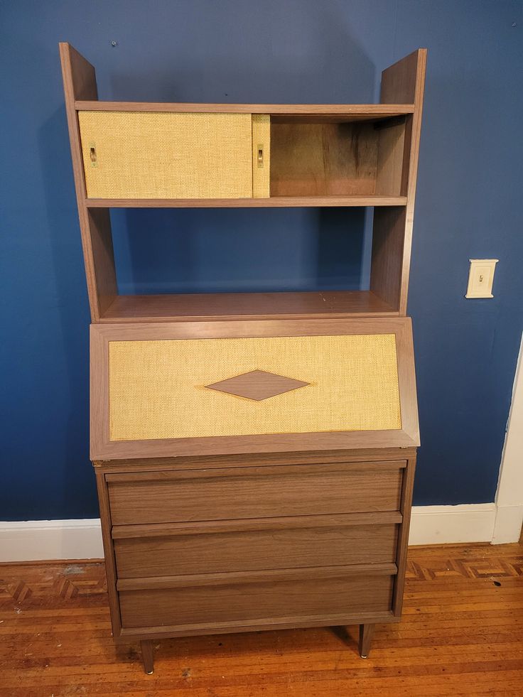 a wooden desk with two drawers and a shelf on the top, against a blue wall