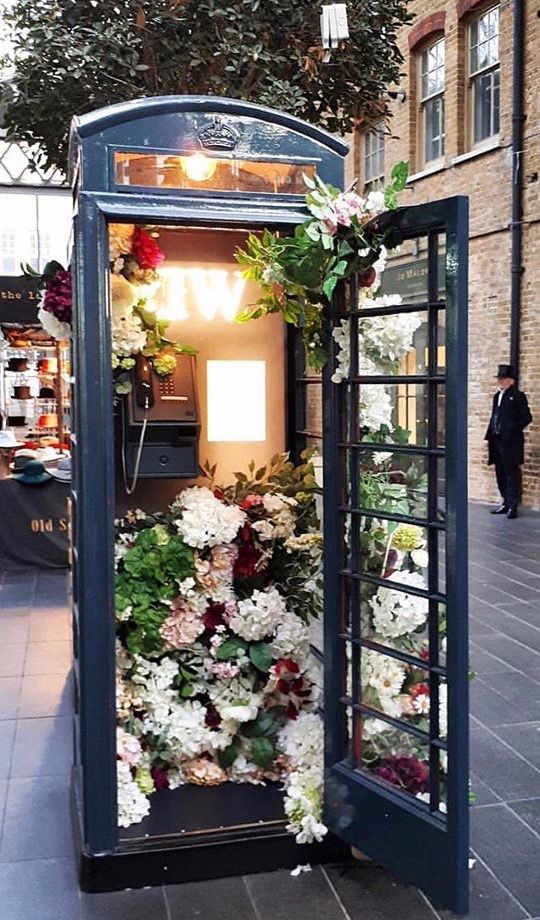 a phone booth with flowers in it on the sidewalk