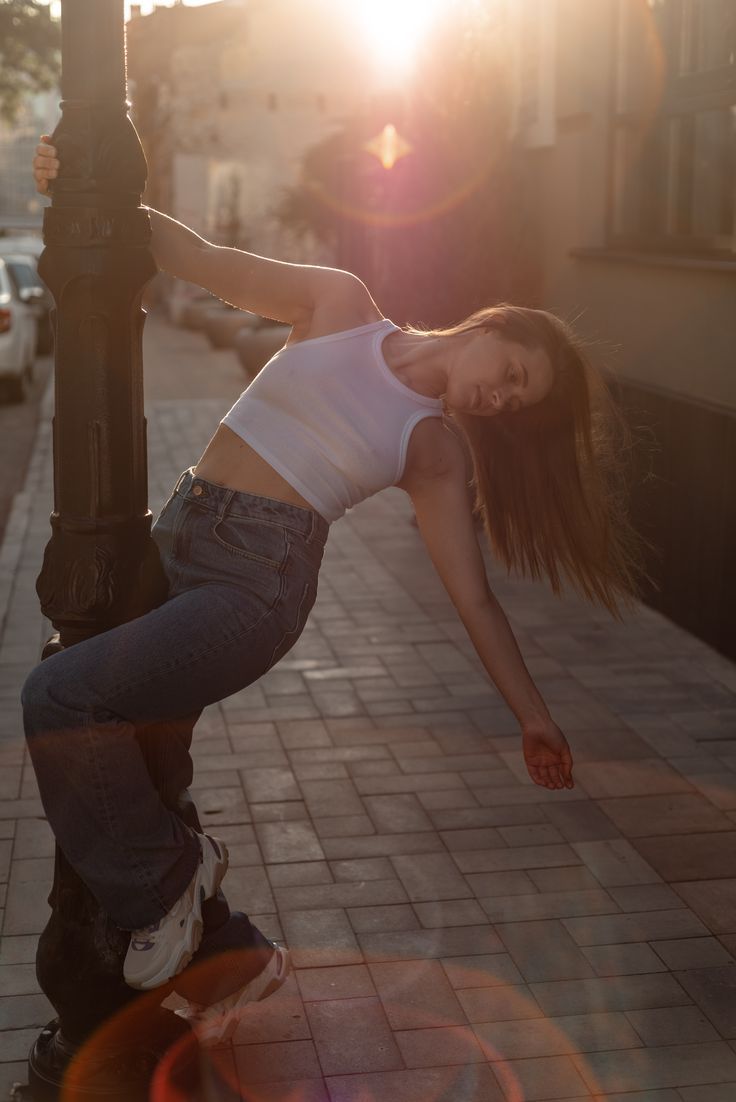 a young woman is leaning on a lamp post and doing a trick with her skateboard