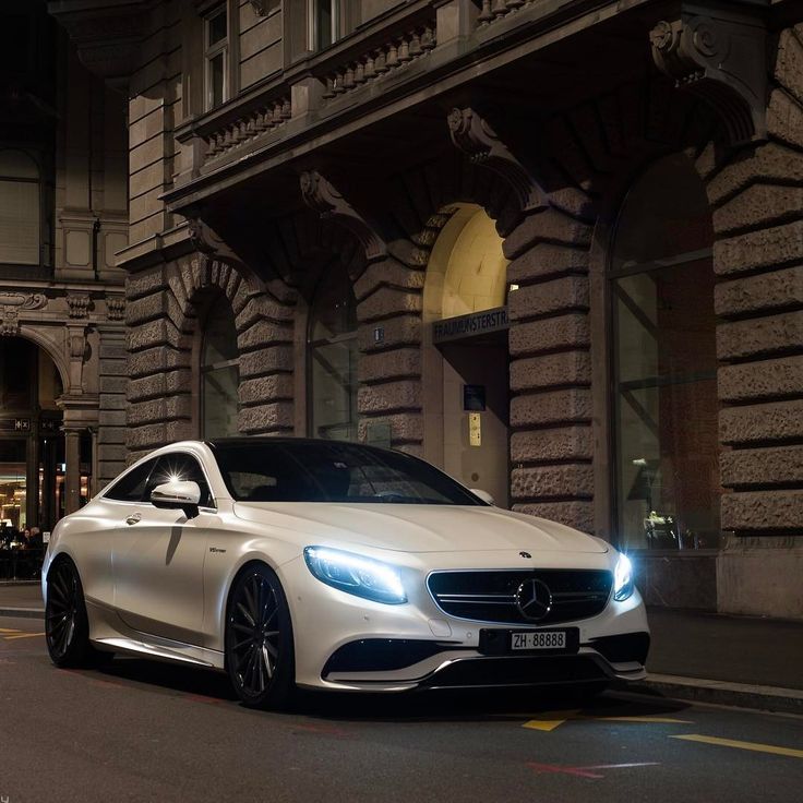 a white mercedes s - class parked on the side of a city street at night