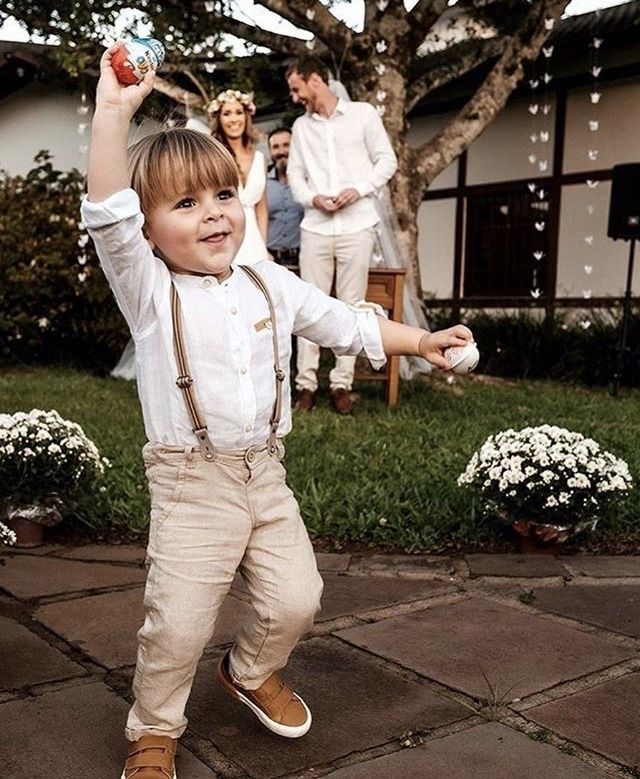 a young boy in suspenders and overalls holds up an apple as people watch