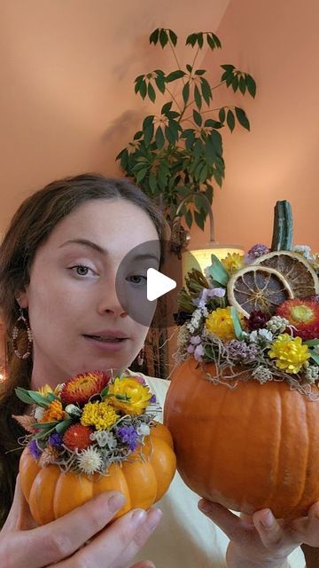 a woman is holding two pumpkins decorated with flowers and foliage in front of her face