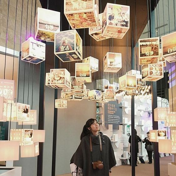 a woman standing in front of a display with many square lights hanging from it's ceiling