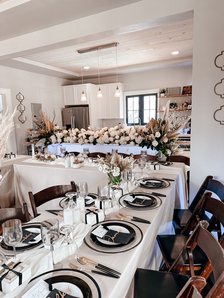 a dining room table is set with black and white plates, silverware, and centerpieces