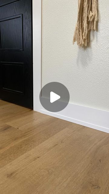 a black door and white wall with a wooden floor in front of it that has a rope hanging from the side