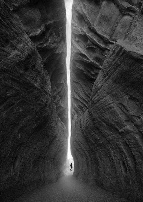 a man is standing in the middle of a narrow tunnel between two large rocks, with one light at the end