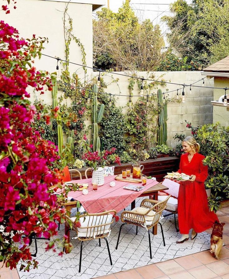 a woman in red jacket sitting at table with flowers and potted plants behind her