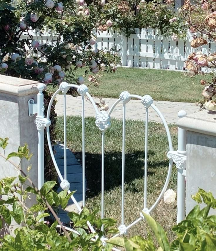 a white iron bed frame sitting in the middle of a yard next to a fence