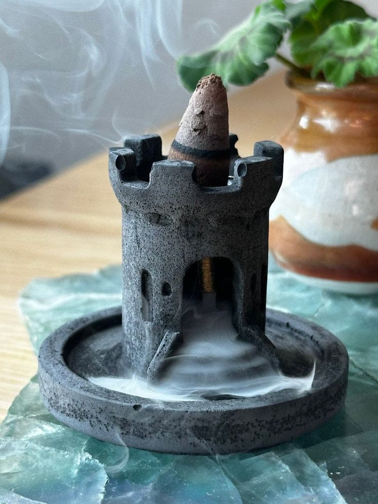 Elevate your space with this handcrafted black concrete medieval castle cone incense holder. Featuring a mesmerizing cascading and pooling smoke effect, this unique incense burner will bring an enchanting atmosphere to any room. This product is designed for use with "backflow" incense cones to create a cascading smoke effect but can also hold standard incense cones. Dimensions: Height: 2 inches Base Diameter: 2.5 inches Material: Concrete Color: Matte black with rustic medieval detailing. Note: Backflow Incense Holder, Cone Incense Holder, Backflow Incense Burner, Chateau Medieval, Cone Incense, Incense Cone, Backflow Incense, Concrete Color, Incense Holders