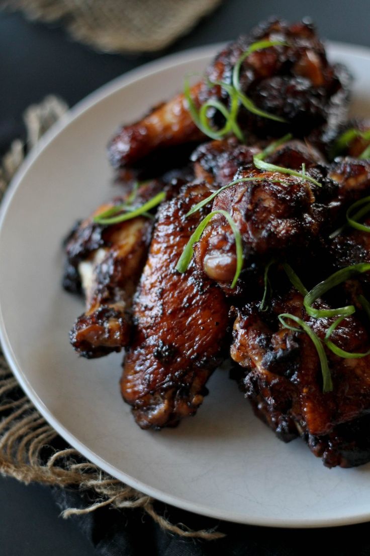 a white plate topped with chicken wings covered in sauce and garnished with scallions