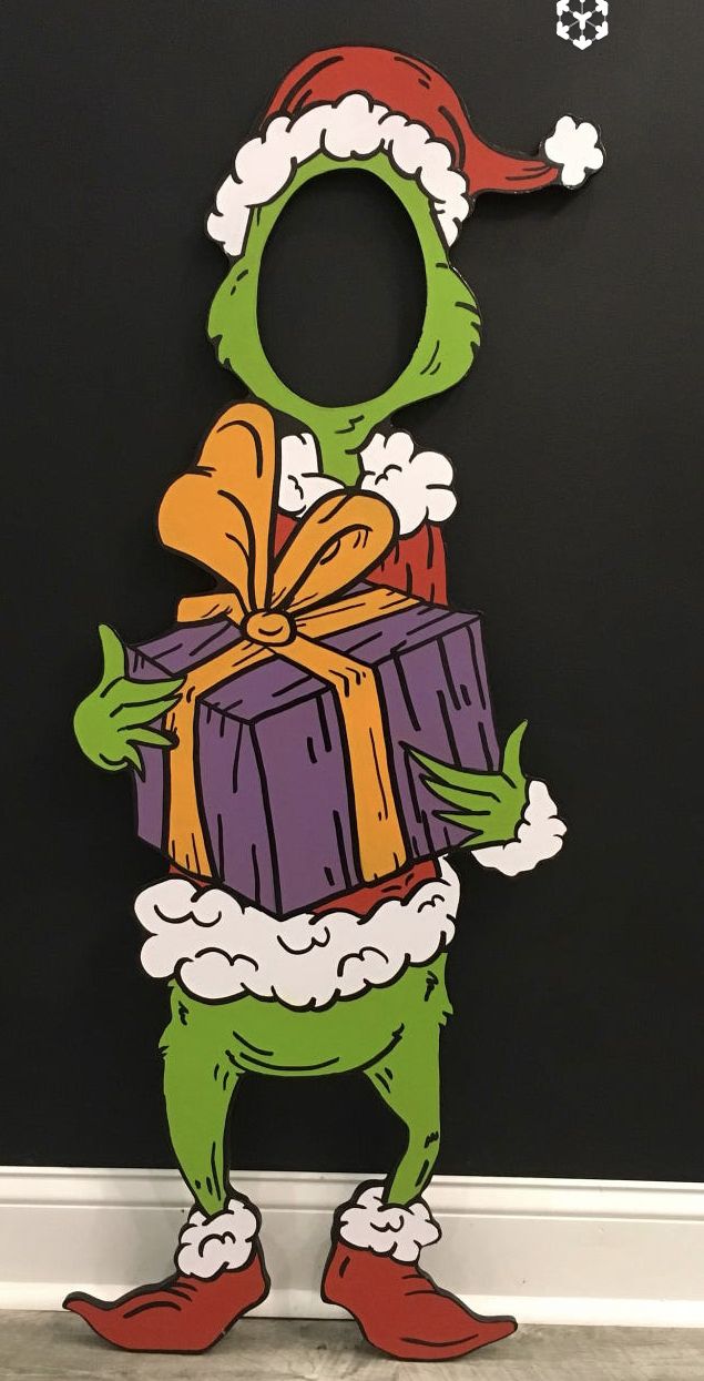 the grinch is holding a christmas present in front of a blackboard with santa's hat on it