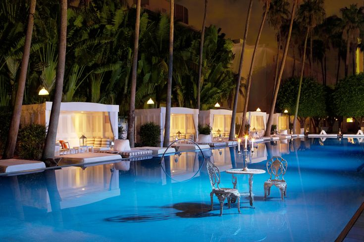 an outdoor pool at night with chairs and tables set up for the guests to enjoy